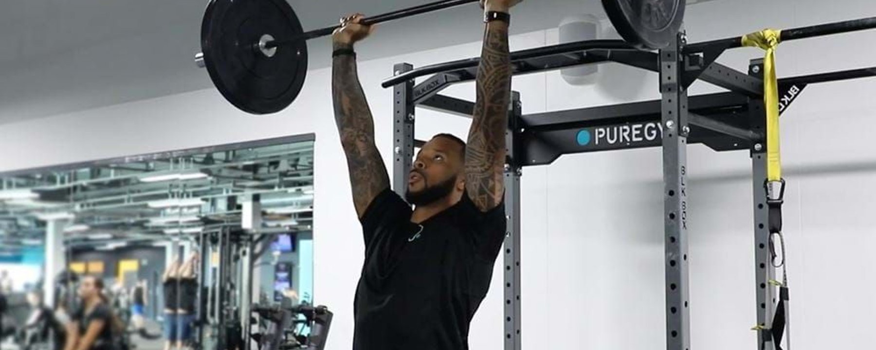 Man lifting barbell overhead in gym with mirrored wall and equipment in background