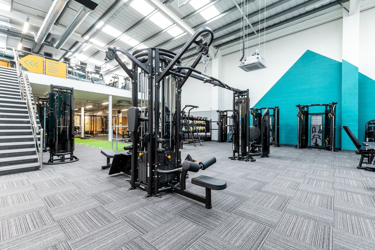 PureGym Chippenham: Weight machines, functional trainers, turf area, rubberized flooring in an open gym studio.