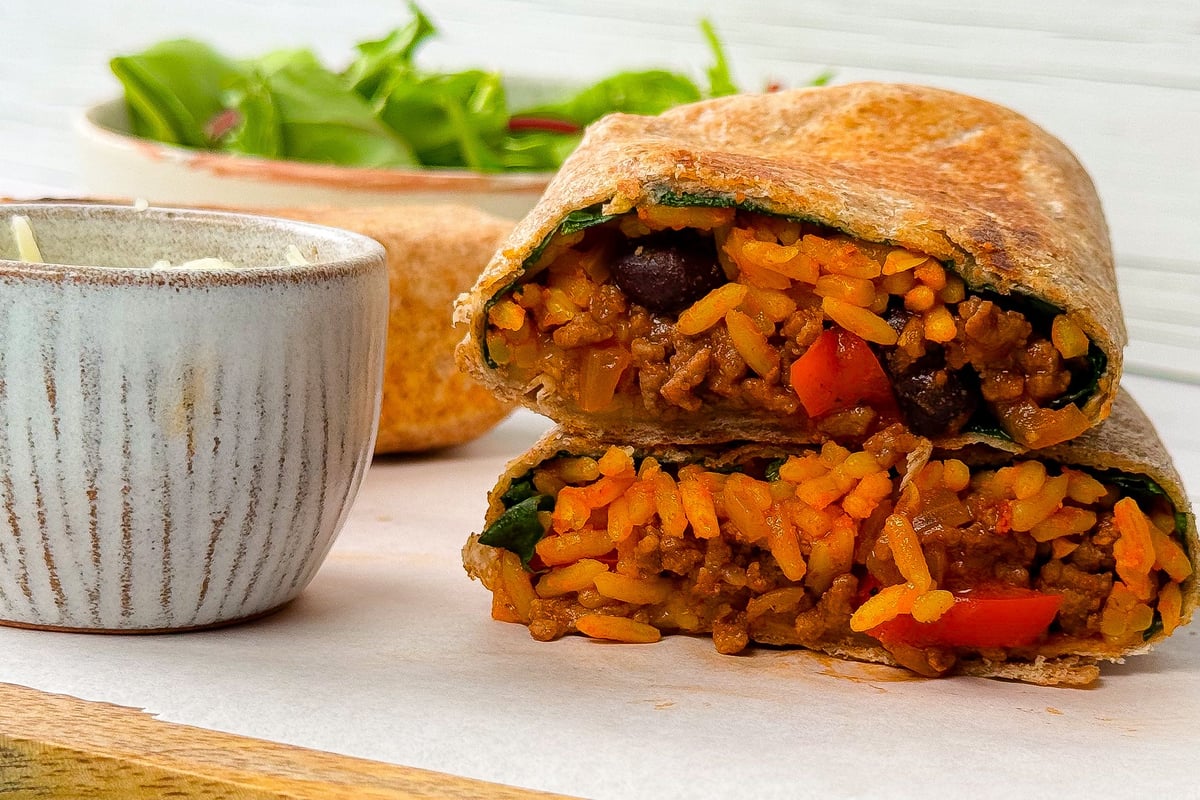Toasted burrito cut in half showing rice, beans and vegetables next to bowl