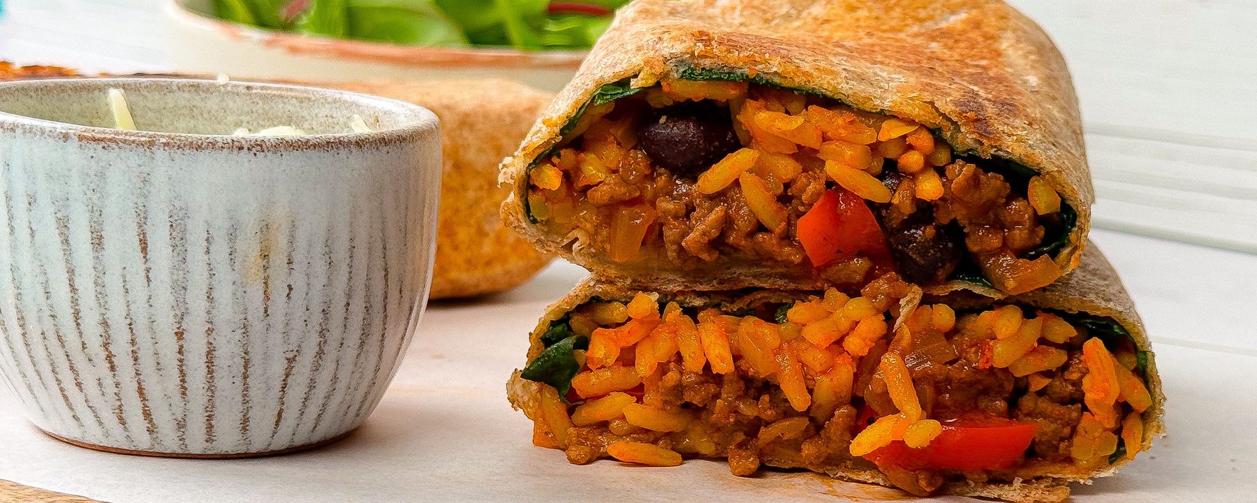 Toasted burrito cut in half showing rice, beans and vegetables next to bowl