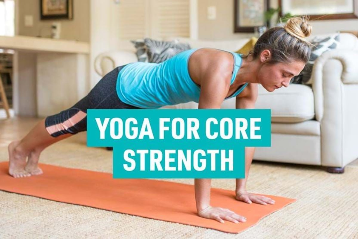 Woman in blue top and black leggings doing plank pose on orange yoga mat indoors