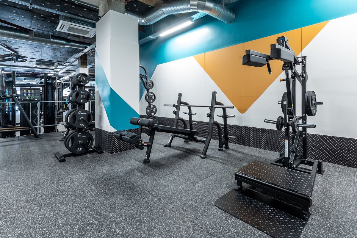 PureGym London Beckenham: Weight benches, squat racks, barbells, weight plates, rubberized floor in a modern gym space.