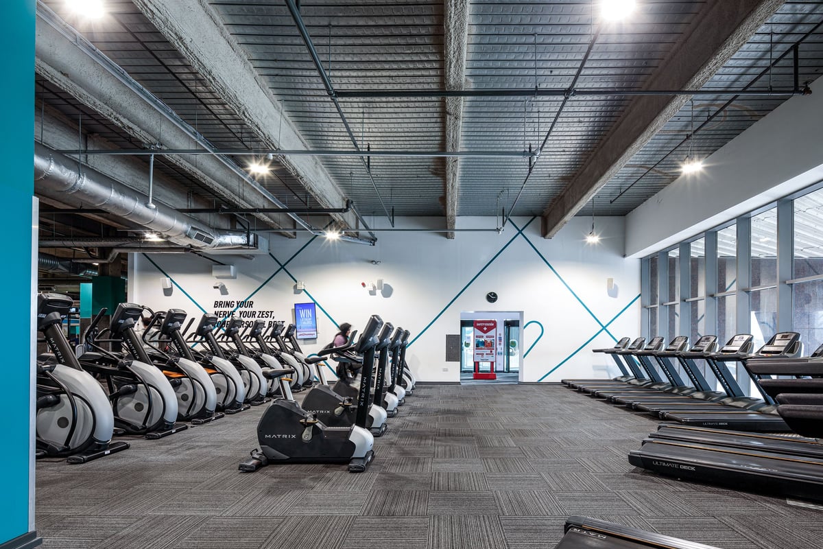 PureGym Cardiff Central: Rows of treadmills, exercise bikes, and weight benches in a gym with exposed ceiling beams.