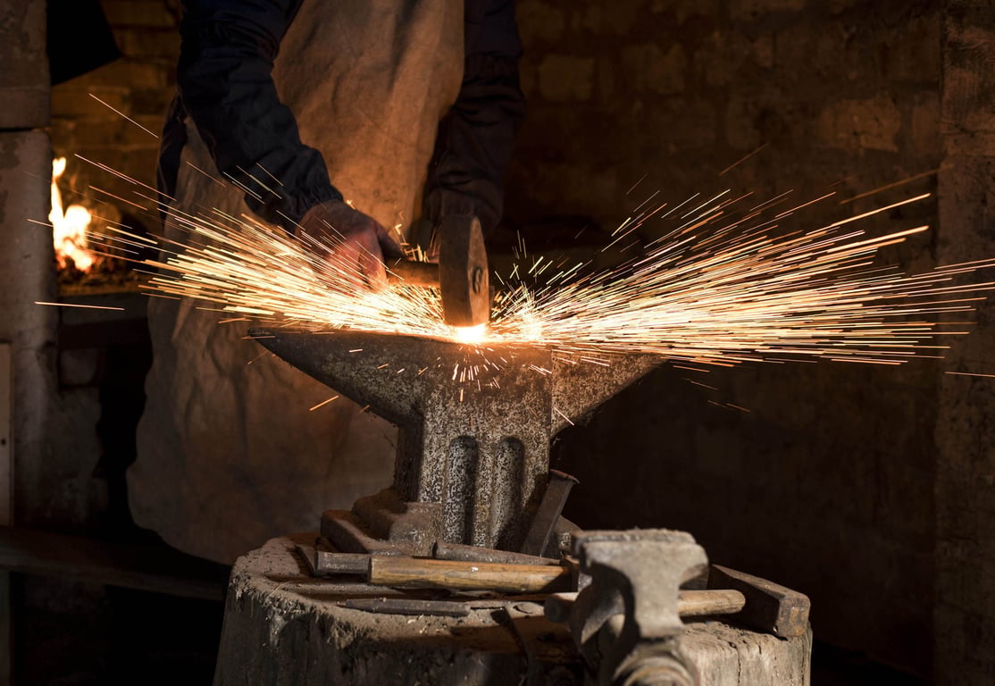 Blacksmith forging metal on anvil