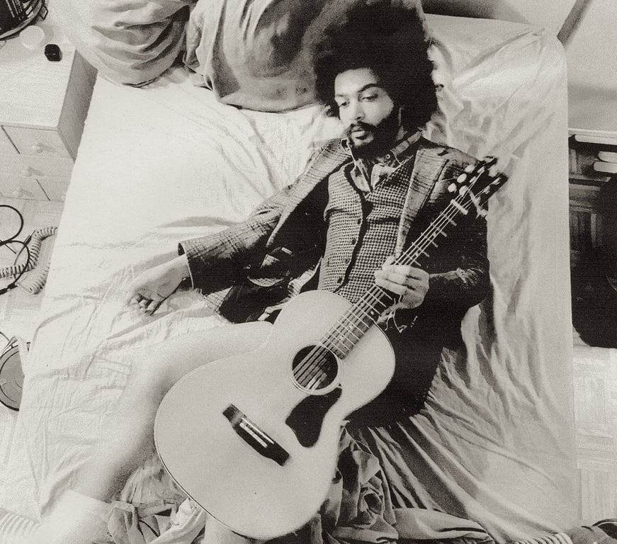 Yves Jarvis lies on a bed with an acoustic guitar