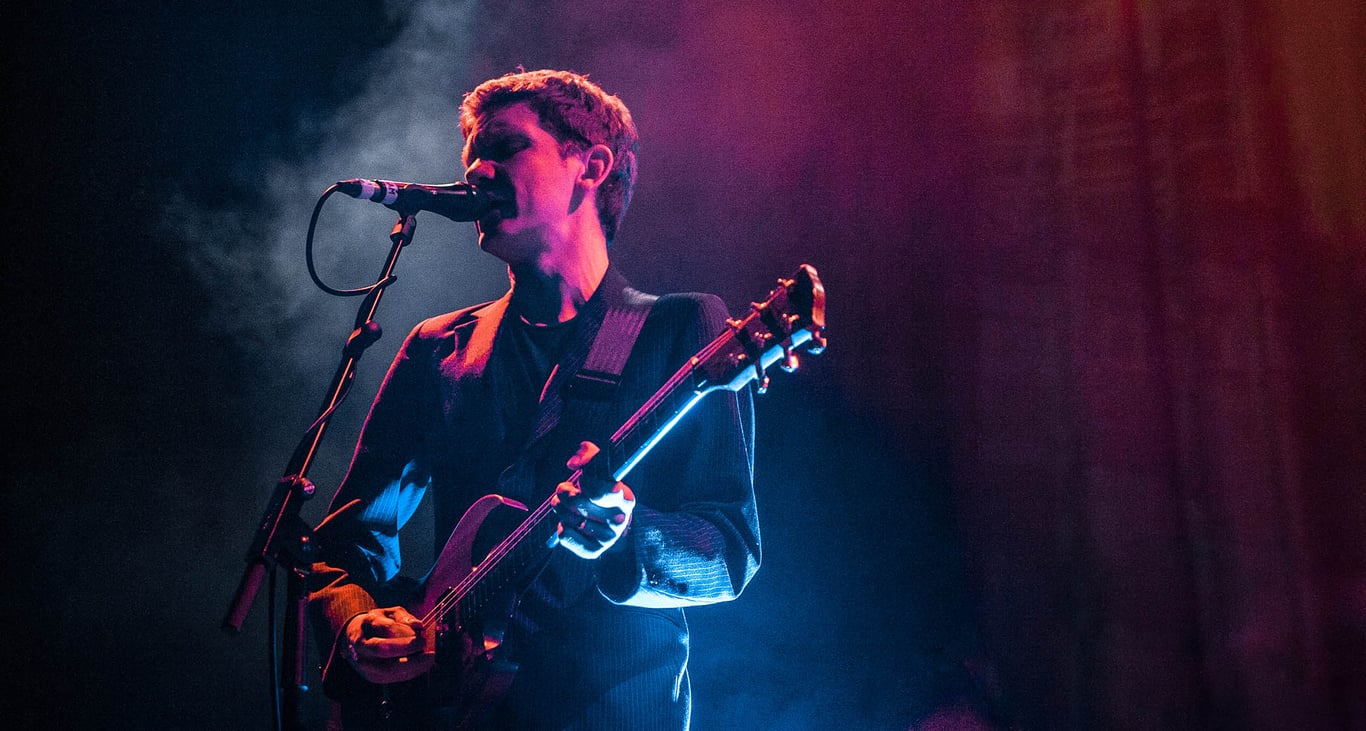 Peter Brewis of Field music is bathed in pink and blue lights as he performs live