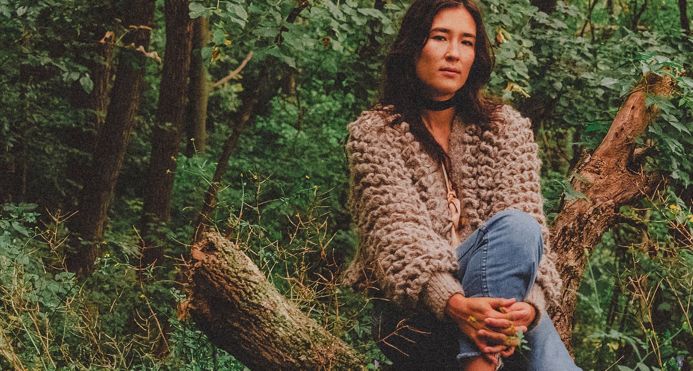 Lea Thomas sits on a log in the forest with her hands clasped round her leg.