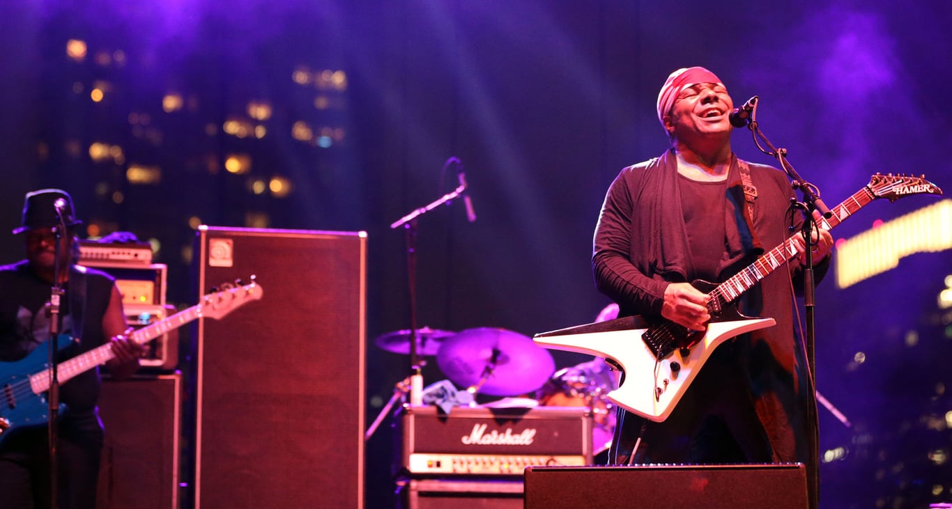 Dez Dickerson wears a red bandana and plays a crazy shaped Hamer electric guitar onstage at a Prince tribute show in 2017