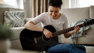 Women sits down playing a black acoustic guitar