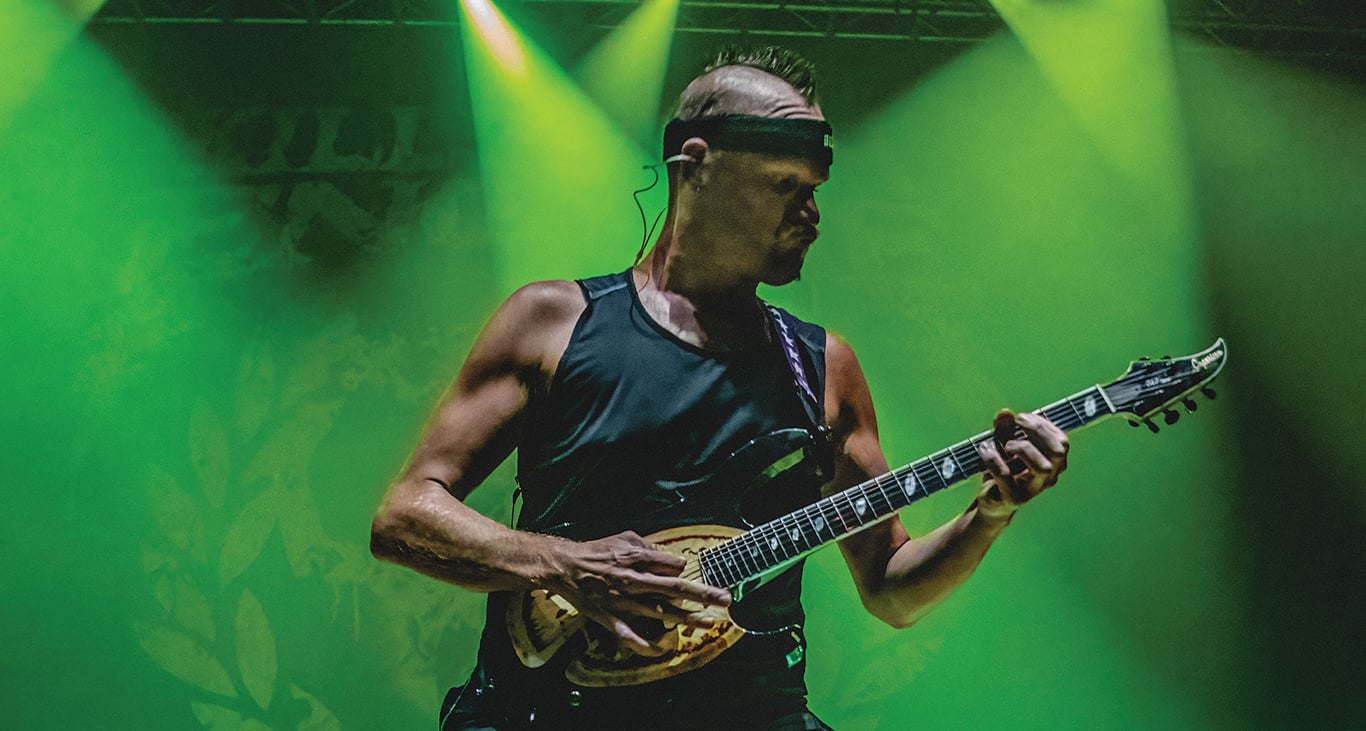 Adam Dutkiewicz of Killswitch Engage rocks a mohican and a Caparison on a stage bathed in green light.
