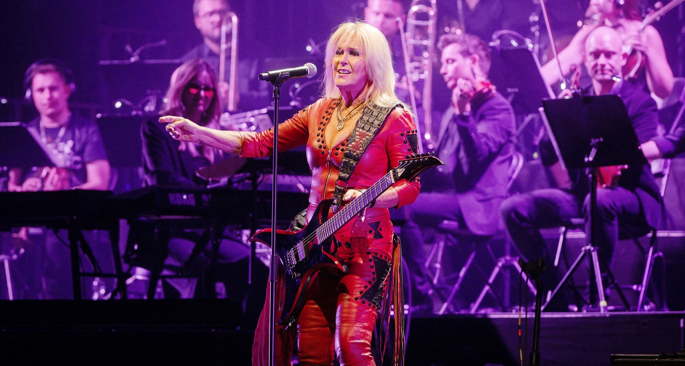Lita Ford is dressed in all red and plays a super-aggressive BC Rich as she performs with an orchestra in the background.