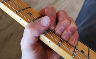Closeup of three fingers on a fretboard and thumb placement
