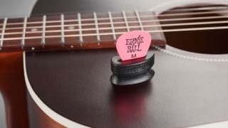 A 'Pick Buddy' guitar pick holder with an Ernie Ball guitar pick attached to the upper bout of an acoustic guitar