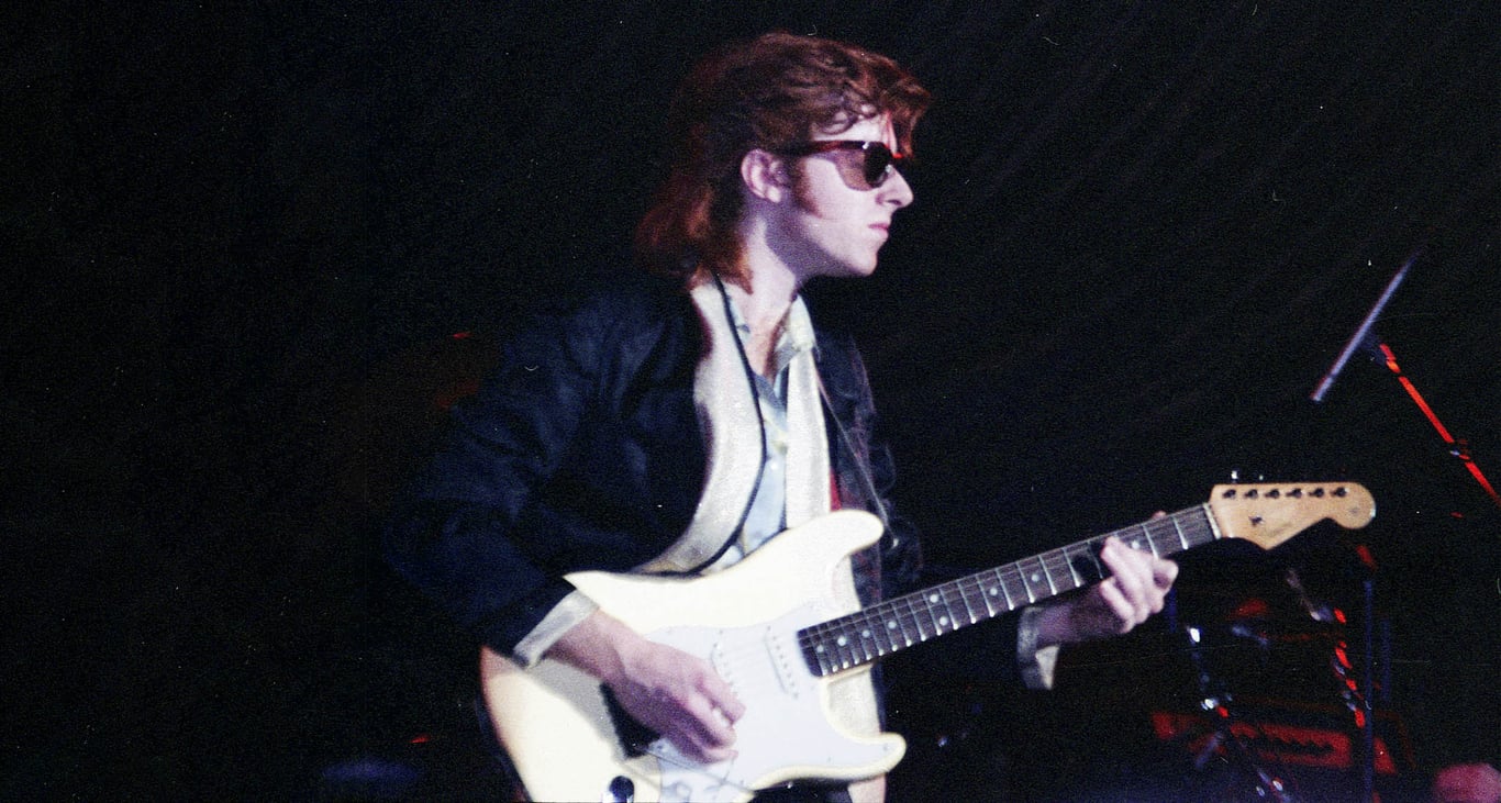 John McCurry performs in the '80s with dark wayfarer sunglasses and an Olympic White Stratocaster.