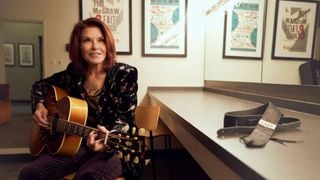 Rosanne Cash playing her Gibson acoustic guitar &ndash; her 'Cash' strap lies beside her on a table