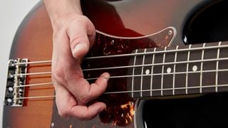 Close up of first finger 'popping' the D string on a bass guitar