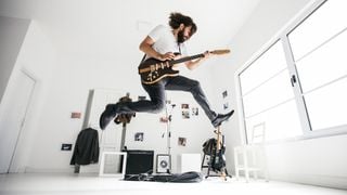 Man in white t-shirt and playing electric guitar leaps high in the air