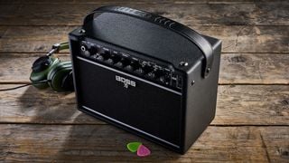 Boss Katana Mini X amp on a wooden floor next to green headphones and some guitar picks