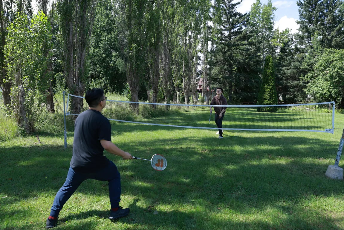 Deux personnes jouent au badminton sur une pelouse entourée d’arbres