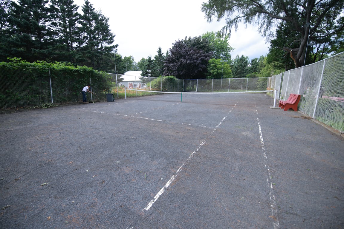 Terrain de tennis extérieur clôturé, entouré d’arbres sur le terrain de l’hôtel
