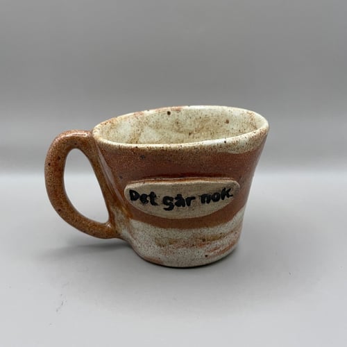 Kop med tekst “Det går nok” i brune nuancer