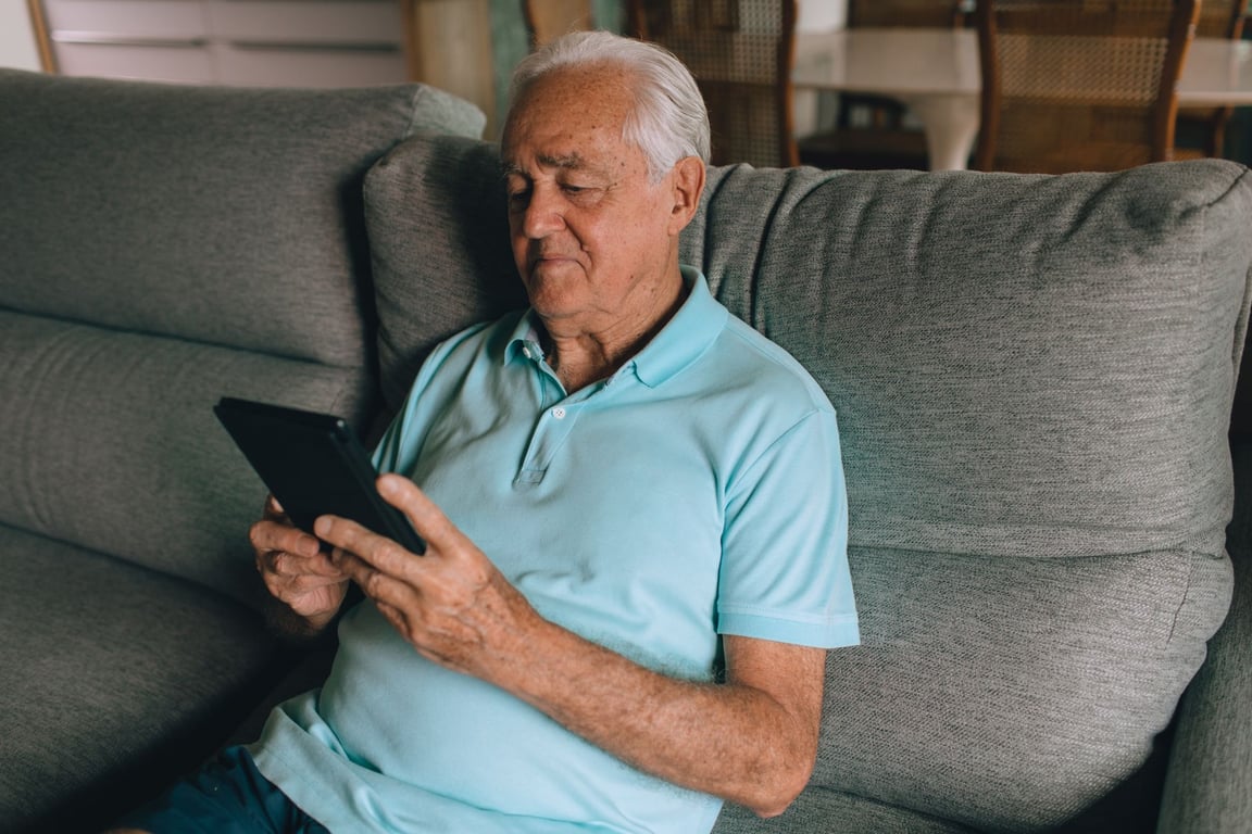 Elderly man relaxing on a sofa using a tablet device
