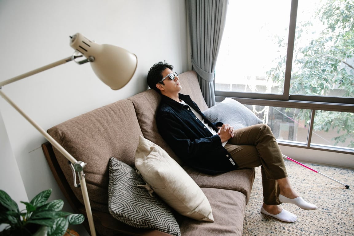 소파에 앉아 휴식하는 동아시아 남성, 팔받침 쿠션 사용을 연상시키는 실내 모습
