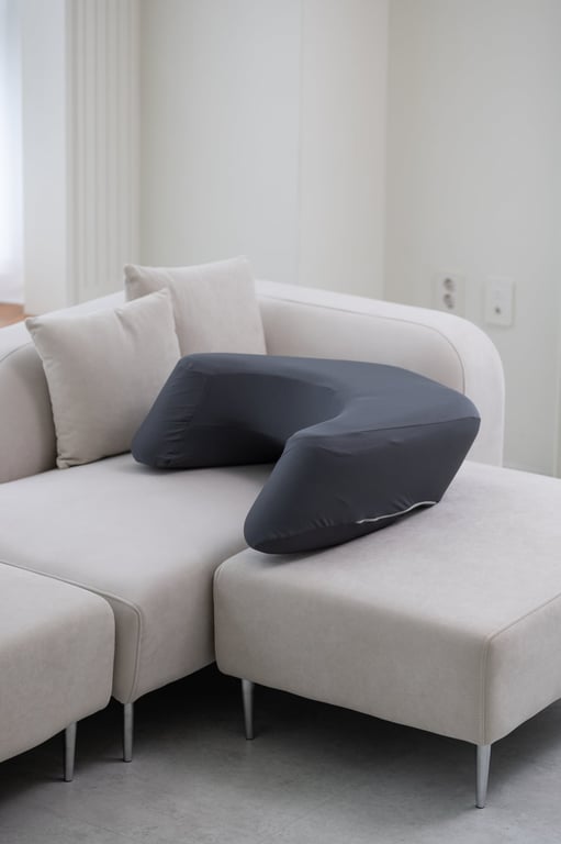 Dark gray LevelUp Cushion nestled between a modern white lounge sofa and footrest, highlighting its ergonomic fit in a minimalist living space