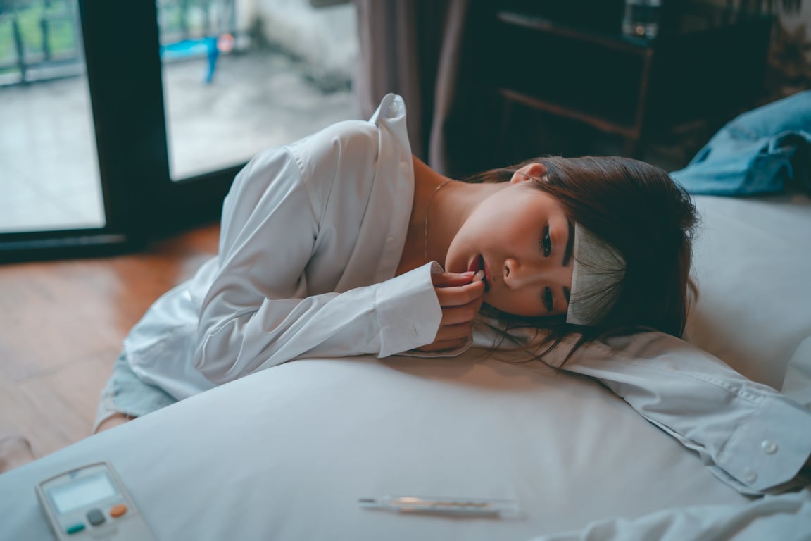 침대에 누워 몸이 불편한 듯한 표정을 짓고 있는 여성