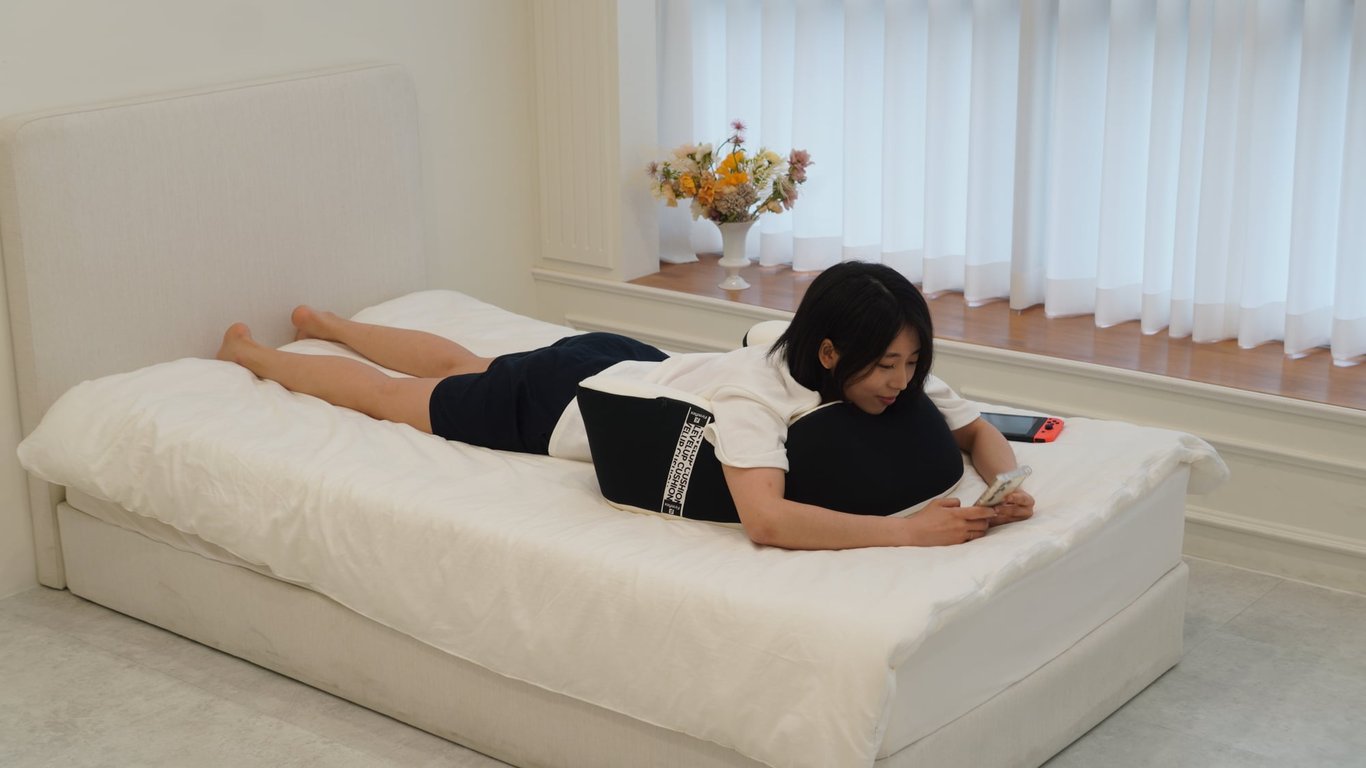 침대 위에 엎드려 팔 아래 레벨업쿠션을 받치고 스마트폰을 보는 여성