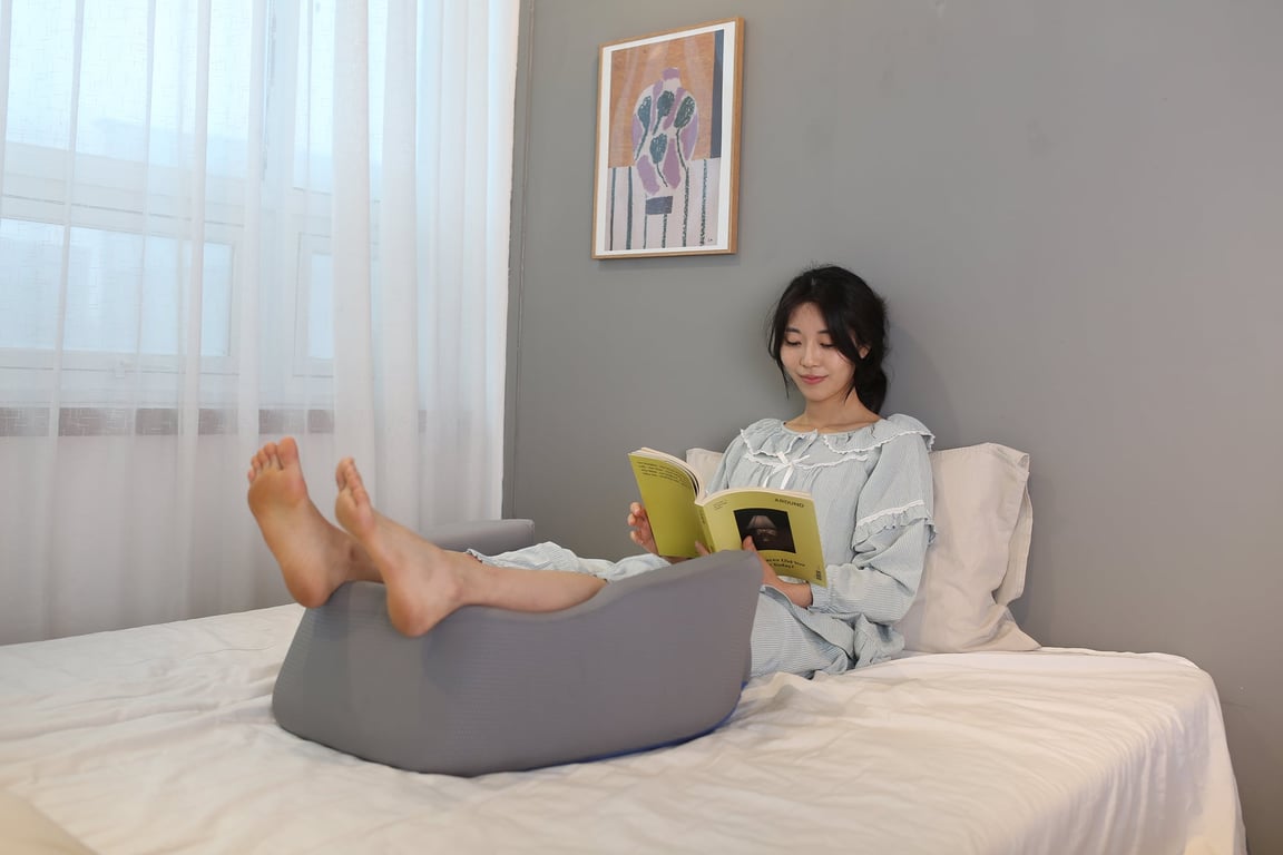 A close-up of legs resting on the FIRMFLEX LevelUp Cushion placed under the knees while lying in bed