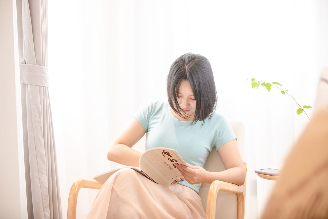 明るいリビングで本を読んでくつろぐアジア系女性