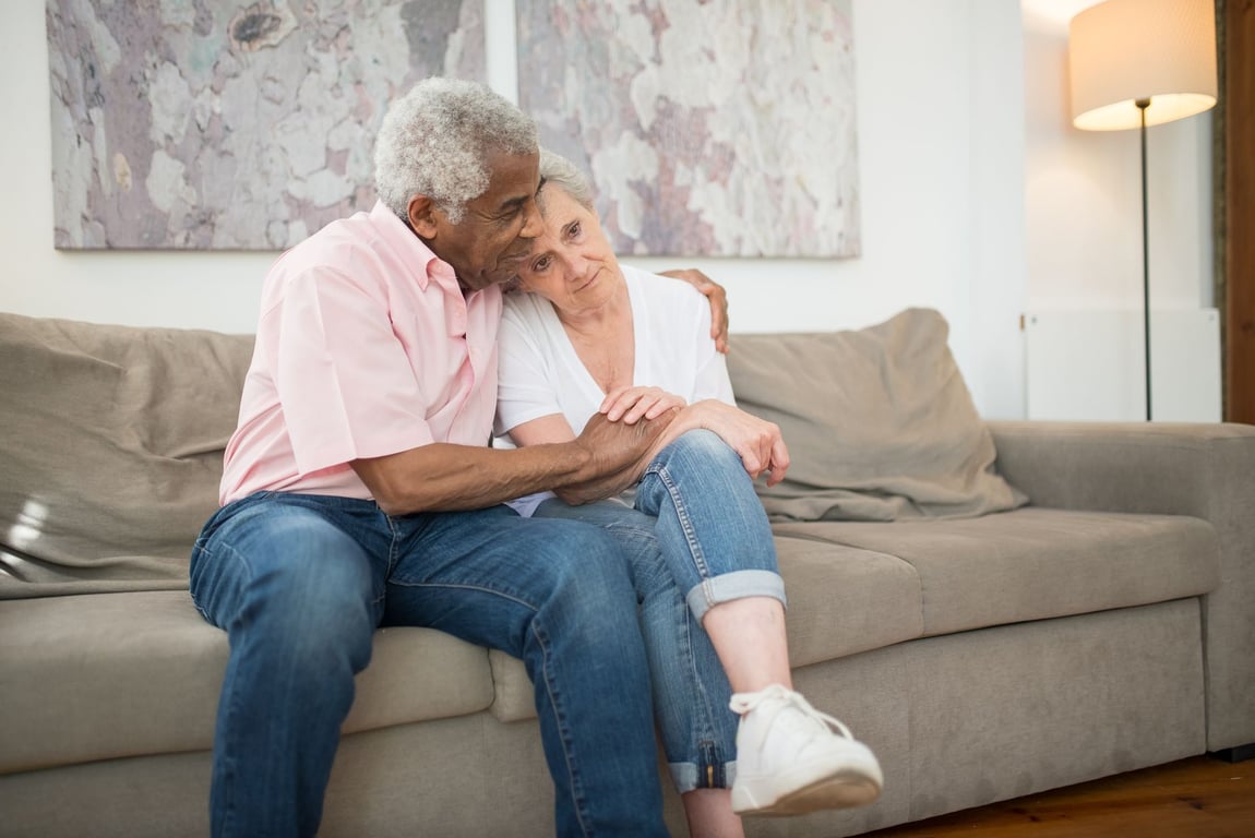 Senior couple embracing warmly on a sofa at home, showcasing love and togetherness in a comfortable living room.