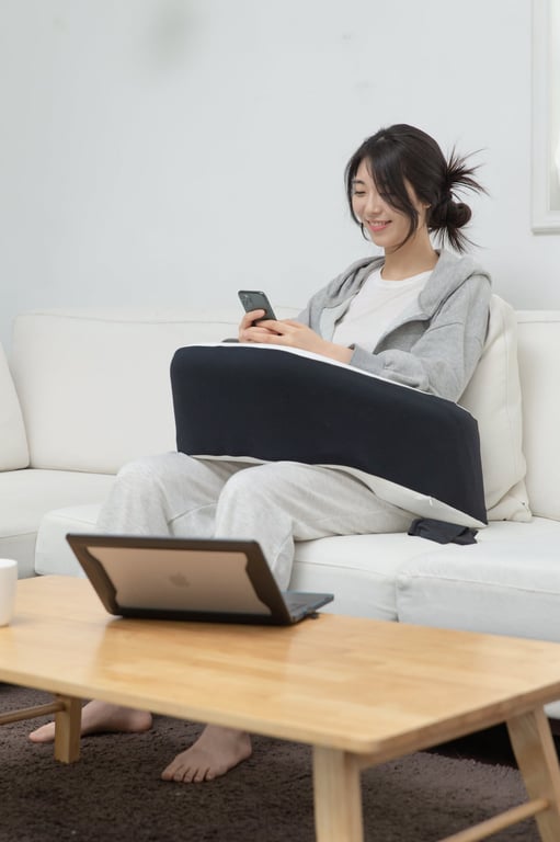 20대 여성이 흰색 소파에 앉아 검정·흰색 레벨업쿠션을 양팔 아래에 올려 팔을 편안하게 받치며 스마트폰을 보고 있는 장면