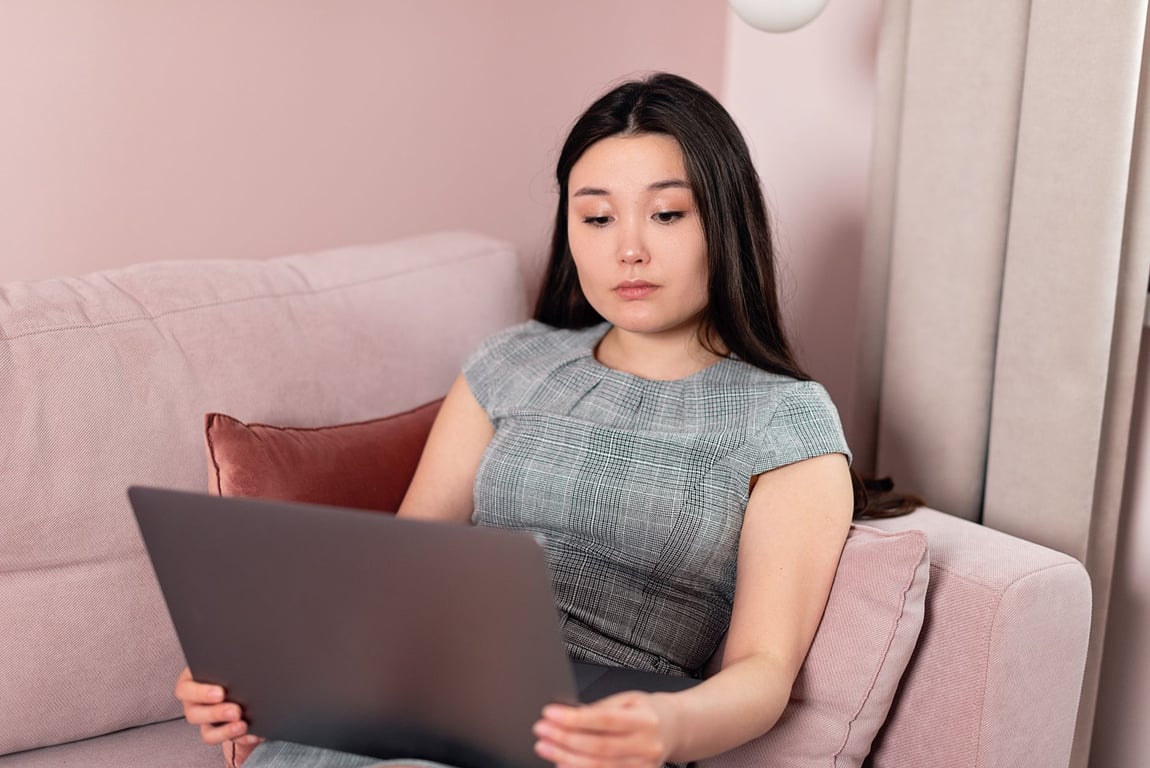 年轻女性坐在粉色沙发上使用笔记本电脑进行远程办公