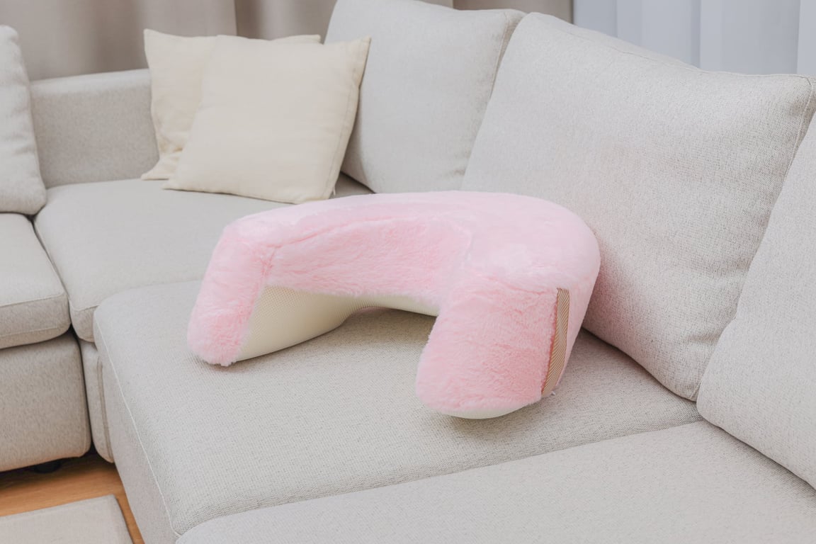 연한 분홍색 토끼털 소재의 레벨업쿠션이 밝고 깔끔한 베이지색 소파 위에 놓여 부드러운 질감과温馨한 분위기를 연출합니다.