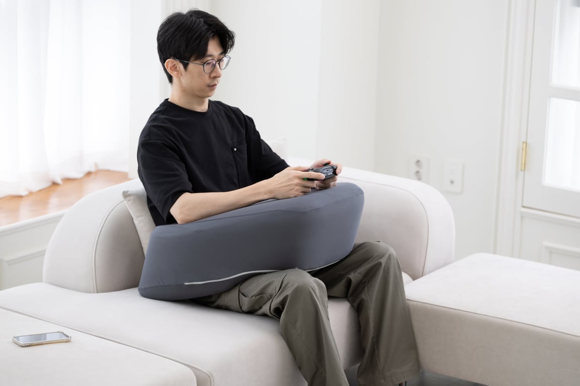 다크 그레이 레벨업쿠션 위에 게임 컨트롤러를 들고 앉아 팔을 안정적으로 받치고 있는 남성의 모습