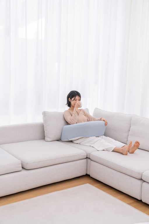 허리에 연한 블루 컬러 레벨업쿠션을 대고 회색 소파에서 편안하게 휴식을 취하는 짧은 머리의 젊은 여성