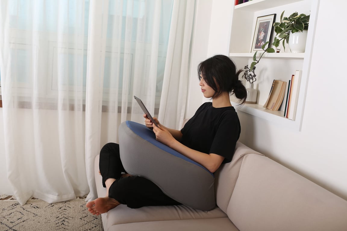 ソファに座った女性がレベルアップクッションをひざの上に置き、タブレットを快適に支えている様子