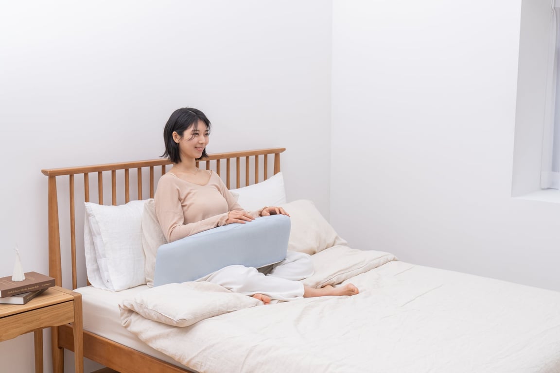 A woman relaxing in bed with the light blue LevelUp Cushion under her knees, enjoying a comfortable resting position.