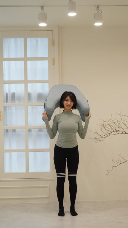 グレーのレベルアップクッションを肩に乗せて立っている若い女性。製品の形状とサイズ感を強調