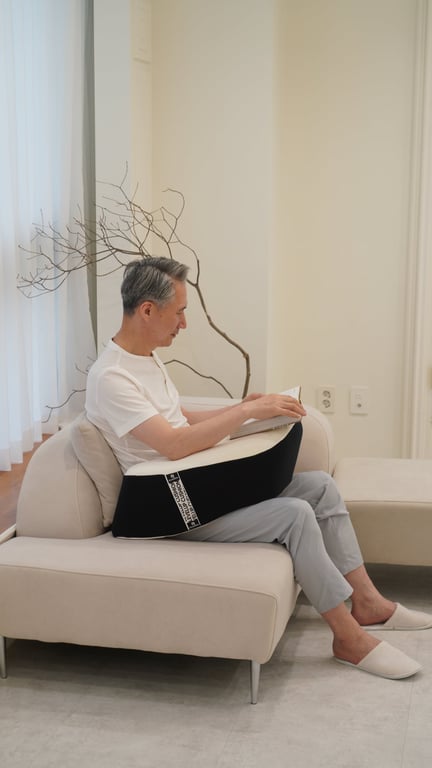베이지색 소파에 앉아 레벨업쿠션 위에 팔을 올리고 책을 읽고 있는 중년 남성