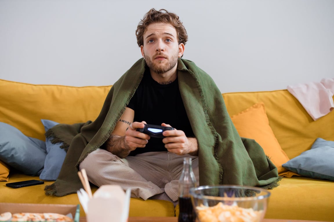 毛布に包まれて快適な雰囲気の中でコントローラーを持ってゲームをする男性