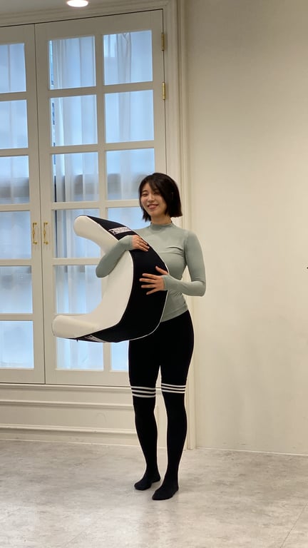 밝은 스튜디오에서 검은색과 흰색 레벨업쿠션을 들고 제품의 크기와 곡선 디자인을 강조하는 여성.