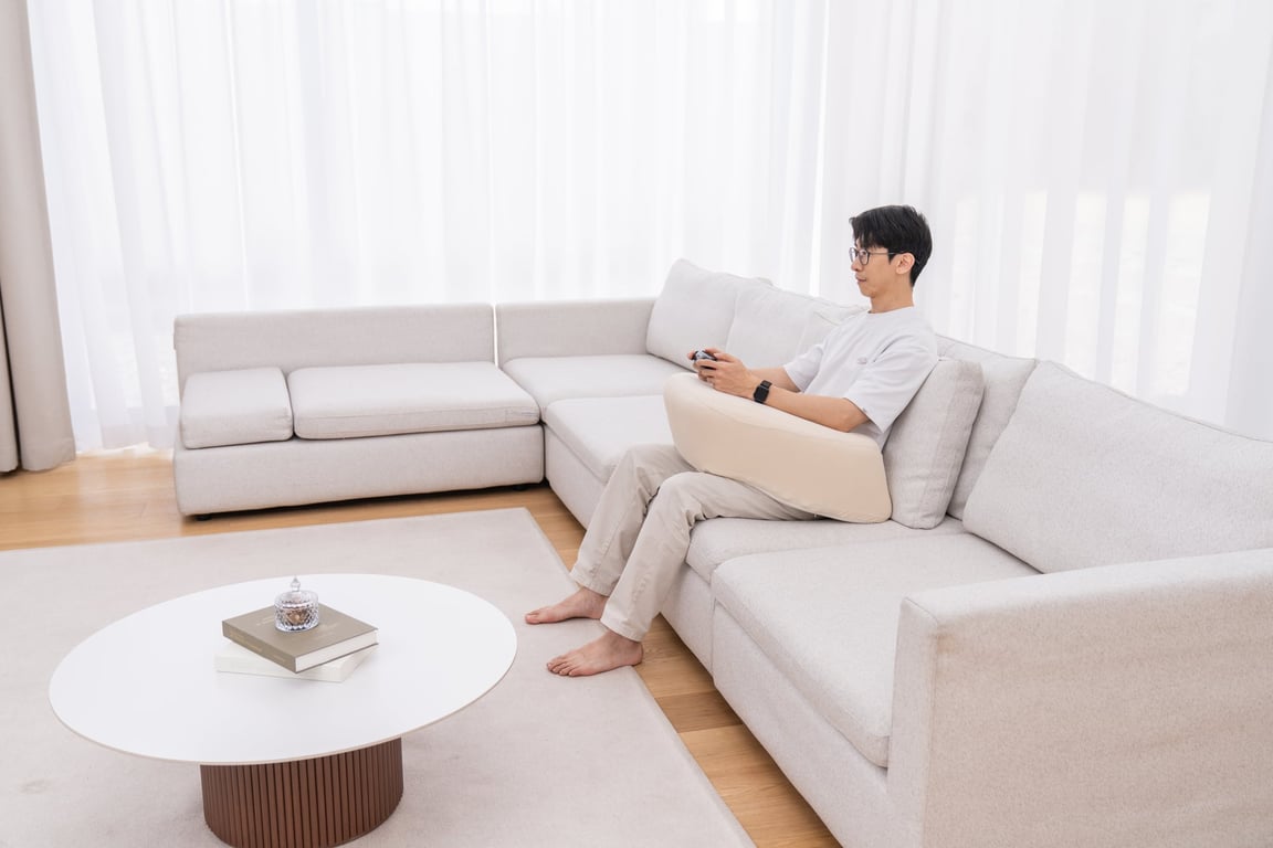 A gamer resting their elbows on the beige LevelUp Cushion while holding a controller on a sofa