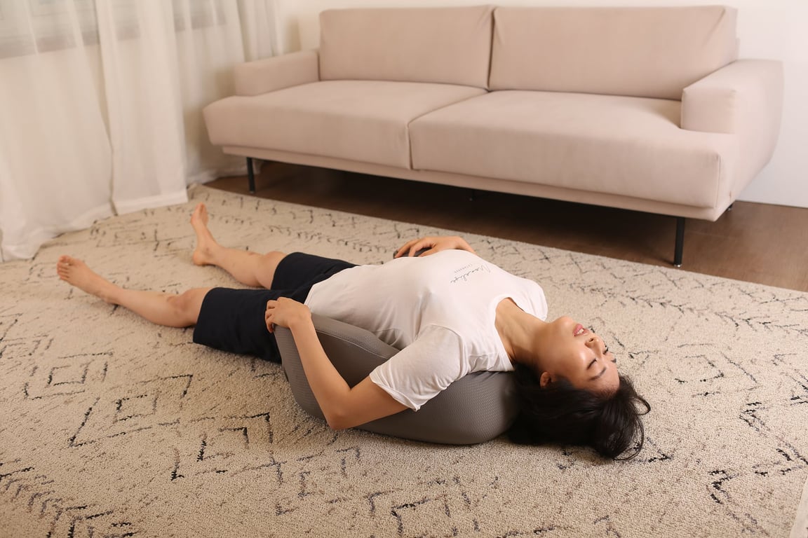 그레이 색상의 레벨업쿠션을 허리 아래에 받치고 바닥에 누워 등을 뒤로 젖히며 스트레칭하는 모습