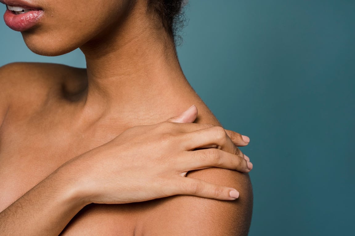 side view of woman touching bare shoulder against blue background
