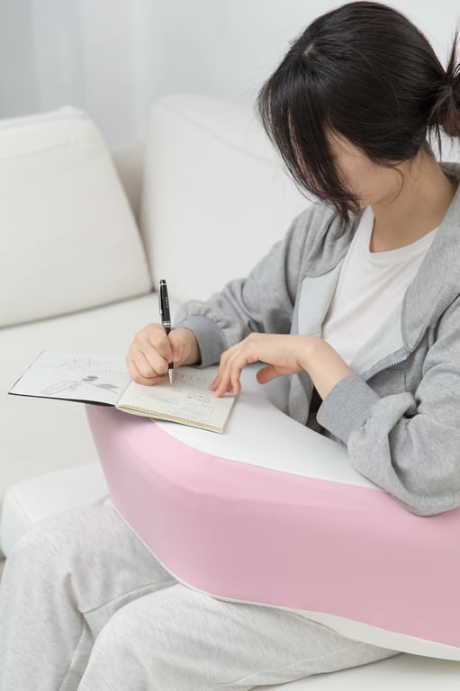 무릎 위에 레벨업쿠션을 올리고 그 위에서 노트에 펜을 들고 집필하는 여성의 팔과 손 부분. 팔꿈치와 손목을 지지하는 쿠션의 역할을 보여줍니다.