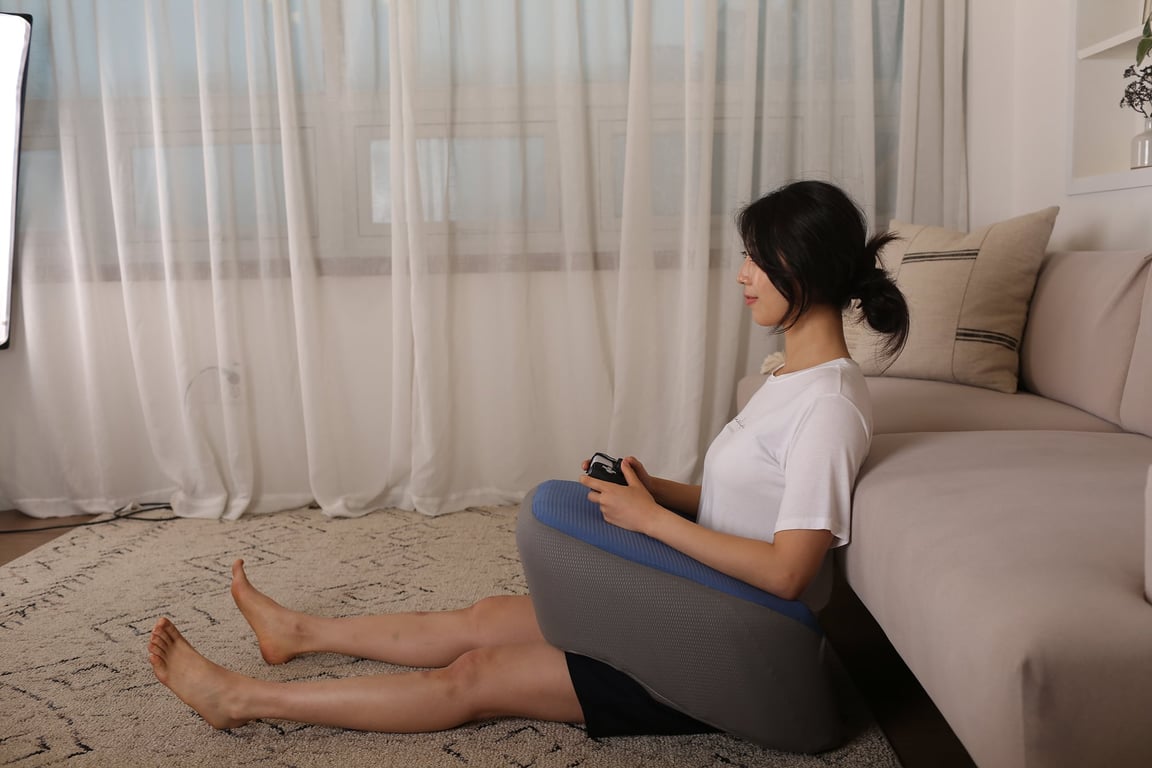 레벨업쿠션을 무릎 위에 올려두고 게임 컨트롤러를 얹은 채 소파 앞 바닥에 앉아 있는 여성의 모습