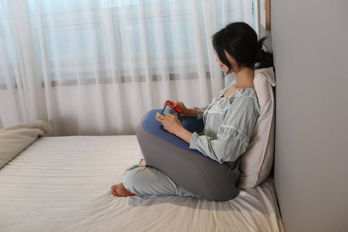 침대 위에서 닌텐도 스위치를 플레이하면서 무릎 위에 레벨업쿠션을 올려 팔을 받치고 있는 모습